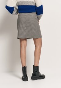 Szara spódnica mini w wzór houndstooth z bocznymi kieszeniami, połączona z błyszczącymi czarnymi botkami za kostkę o masywnej podeszwie i sznurowanym fasonie.