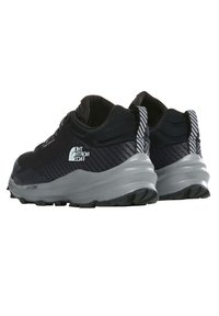 Zapatillas deportivas negras con parte superior texturizada, detalles reflectantes y una suela de amortiguación gris gruesa con un patrón de tracción rugoso.