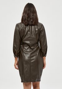 Abito in finta pelle verde oliva scuro con maniche lunghe e leggermente ampie, dalla silhouette aderente. Accentuato da fessure laterali nei polsini.