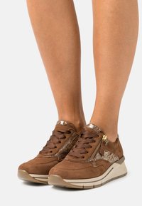 Bruna mockasn sneakers med en glänsande guldaccent, snördesign och en sidogömma, med en vadderad, ljusfärgad sula.