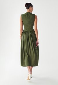 Vestido midi sin mangas en verde oliva, con un corsé ajustado y una cintura fruncida, que presenta una textura sutil y una cremallera cerrada en la parte posterior.