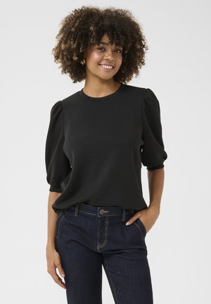 Top nero con maniche a palloncino in tessuto liscio, dotato di scollatura rotonda, abbinato a jeans di denim scuri con cuciture a contrasto e tasche laterali.