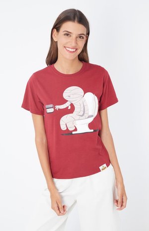 Camiseta de algodón roja con un gráfico de una momia sentada en un inodoro, sosteniendo un rollo de papel higiénico. Diseño de mangas cortas y cuello redondo.