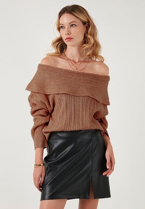 Ruskea ribbed off-shoulder neule, jossa on laskostehty kaula-aukko, yhdistettynä tiukkaan mustaan nahkaminihameeseen, jossa on sivureikä.