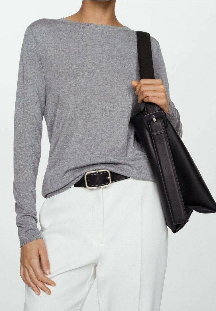 Personne en haut gris à manches longues et pantalon blanc tenant un sac à main en cuir noir avec une boucle de ceinture argentée visible.