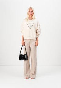 Felpa beige con un design triangolare e decorazioni, abbinata a pantaloni a gamba larga beige chiaro e una borsa nera.