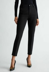 Pantaloni neri su misura con una vestibilità slim, frontale piatto e dettagli di pieghe sottili. Abbinati a tacchi a punta neri con accenti in hardware dorato.