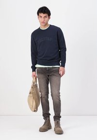 Felpa navy con logo in rilievo, colletto verde chiaro, jeans grigi, borsa beige e stivali color marrone chiaro. Design semplice e casual con texture varie.