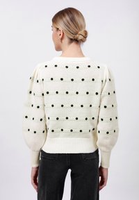 Sweter dzianinowy w kolorze kremowym z ciemnozielonymi kropkami. Bufiaste rękawy i ribbony u dołu. Miękka tekstura, okrągły dekolt i luźny krój.