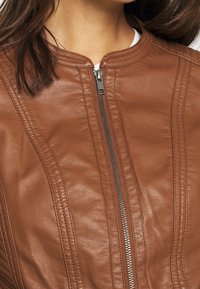 Giacca in pelle marrone con colletto rotondo, zip argentata e dettagli di cucitura verticale. La texture è liscia e morbida.