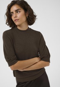 Olive green short-sleeve sweater with a high neckline and gathered detailing at the sleeves, made from a textured knit material.