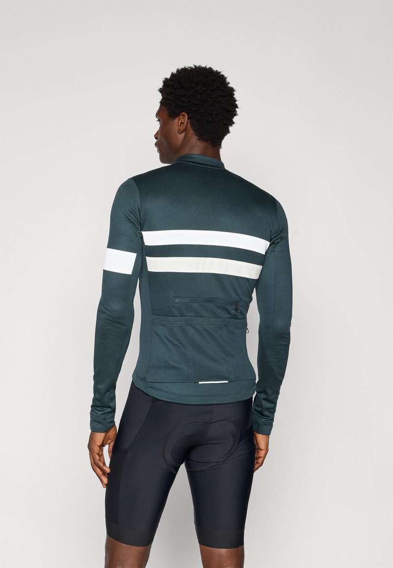 Long-sleeve cycling jersey in dark teal with white stripes, featuring a back pocket and a fitted design. Worn with black cycling shorts.