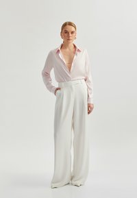 Light pink silk blouse with a deep v-neck, paired with white wide-leg trousers featuring a high waist and belt loops. Smooth textures visible.