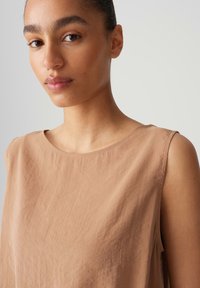 Top senza maniche color sabbia con scollo rotondo, realizzato in tessuto leggero con una sottile texture e dettagli di cucitura puliti.