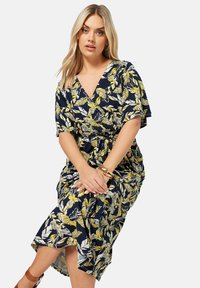 Blommig omlottklänning i marinblått med gula och vita bladmönster. Korta ärmar, V-ringning, midjebälte och knälängd med en sidoflik.