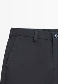Svarta byxor med slät front, två sidofickor, knappstängning och en mjuk tygstruktur. Midjebandet har hällor för bälte.
