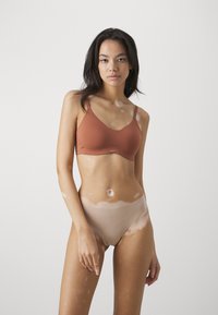 Bruine naadloze bh met verstelbare bandjes, gecombineerd met huidskleurige high-waisted slipjes. Glad textuur, minimalistisch ontwerp en geen zichtbare naden.