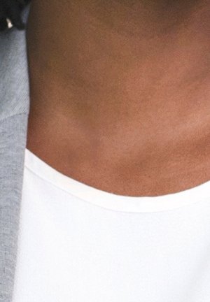 Gros plan sur le cou et le haut de la poitrine d'une personne portant une chemise blanche et un vêtement extérieur gris.