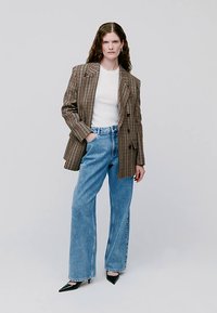 Blazer oversize a cuadros en marrón y beige, combinado con una camiseta blanca y jeans de tiro alto en azul claro. Zapatos de tacón negros con punta en forma de pico completan el conjunto.