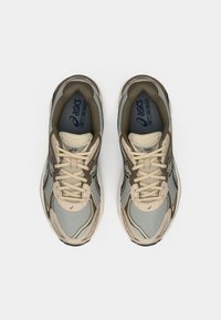 Μπεζ και μπλε πλέκτες αθλητικά παπούτσια με κρεμ κορδόνια, υφασμάτινα πάνελ και μαλακή σόλα. Διαθέτουν το λογότυπο ASICS σε εμφανές σημείο στη γλώσσα.