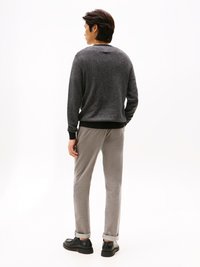 Maglione grigio a maglia con scollo tondo, abbinato a pantaloni grigi chiari e scarpe nere. Tessuto liscio con polsini arrotolati sui pantaloni.