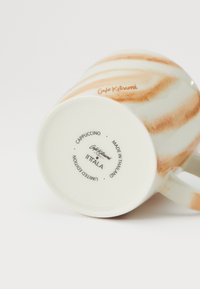 Keramický hrnček na kapučíno s oranžovými a bielymi pruhmi s hladkou textúrou. Na dne sú uvedené značky a informácie o "limitovanej edícii".