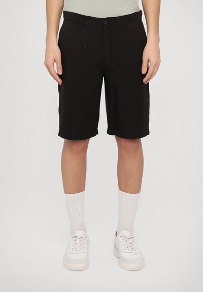 Pantaloni corti neri in cotone, di lunghezza al ginocchio, con chiusura frontale a bottone e tasche laterali, abbinati a calzini bianchi e sneakers.