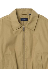 Chaqueta topo con cuello, cierre completo y dos bolsillos laterales. La tela parece suave, con detalles de costura mínimos. Etiqueta de la marca visible.