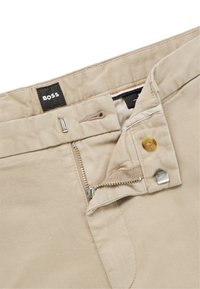 Beige cotton trousers with a zip fly, button closure, and a black "BOSS" label on the waistband. Features metal accents and smooth texture.