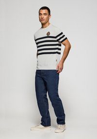 Randig kortärmad tröja i ljusgrått och marinblått, med rund halsringning. Kombinerad med mörkblå jeans och beige sneakers.