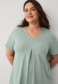Lys grøn kortærmet t-shirt med V-hals og en central plissé, lavet af blødt stof med en glat overflade og minimal detaljering.