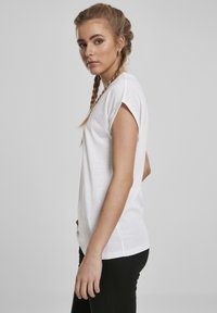 Valge lühikeste varrukatega T-särk pehmest kangast, lõdva istuvuse ja ümarate servadega, kombineeritud mustade kitsaste pükstega.