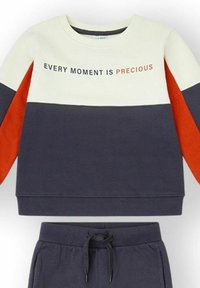 Conjunto deportivo de dos piezas con diseño de bloques de color crema, azul marino y naranja. La sudadera tiene la frase "CADA MOMENTO ES PRECIOSO" impresa en el frente.