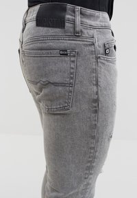 Gros plan sur un jean en denim gris clair avec poche arrière, passants de ceinture, poche latérale et étiquette de marque noire indiquant Big Star.