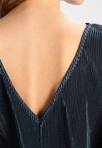 Vestito blu navy con scollatura a V profonda, caratterizzato da una texture a costine e una leggera lucentezza, che mette in mostra una schiena liscia. Accentuato da cuciture visibili.