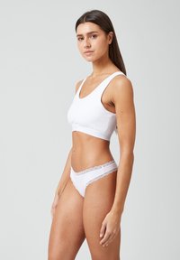 Witte katoenen sportbeha met brede banden en een ronde hals, gecombineerd met bijpassende witte thong met kantafwerking. Gladde textuur, minimalistisch ontwerp.