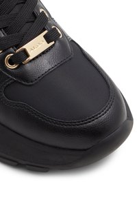 Svart idrottssko med en texturerad ovandel av läder och nylon, detaljer i guldton och en tjock svart gummisula.