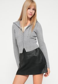 Szara dresowa bluza z kapturem i zamkiem, o skróconym fasonie, zestawiona z czarną mini spódnicą z faux skóry z wzorem w krokodylą skórę.