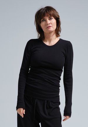 Čierna dlhá rukávová košeľa vyrobená z rebrovaného materiálu, s okrúhlym výstrihom a priliehavým strihom, skombinovaná s voľnými čiernymi nohavicami.