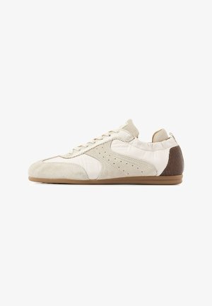 Low-profile off-white sneaker with suede and fabric panels, perforated side details, lace-up closure, and brown textured heel patch.