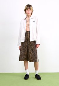 Veste blanche à rayures, shorts en imprimé léopard marron, chaussettes blanches à mi-mollet et baskets noires. Design ajusté avec des éléments contrastants.
