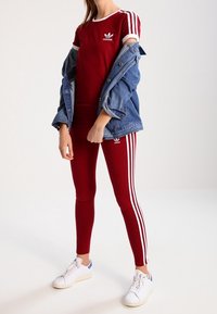 Bordeaux sportkläder med vita randiga detaljer, matchande t-shirt och leggings. Blå denimjacka bars avslappnat, tillsammans med vita sneakers.