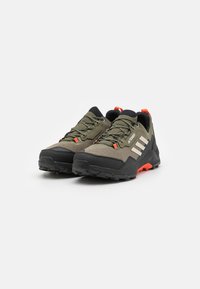 Chaussures d'extérieur en vert olive avec des accents noirs, tige en tissu texturé, bout renforcé et semelle noire robuste avec un détail de talon orange.