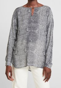 Czarna i biała bluzka z długim rękawem o subtelnym wzorze skóry węża, z wycięciem przy szyi i luźnym krojem.