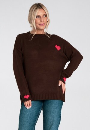 Brązowy sweter z dzianiny z różowymi sercami na klatce piersiowej i rękawach, o luźnym kroju oraz prążkowanym wykończeniu u dołu i na mankietach.