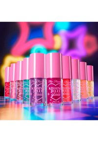 Set van 10 lipglossen van Too Faced in verschillende kleuren, met transparante verpakkingen en roze doppen, gelabeld als "KISSING JELLY gloss."