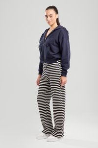 Navy blue zip-up hooded sweatshirt, striped wide-leg pants in navy and cream, paired with white sneakers. Soft fabric, relaxed fit.