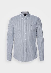 Chemise à manches longues boutonnée avec des rayures verticales bleu marine et blanc et un petit logo sur la poitrine, présentée sur un fond uni.
