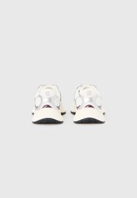 Baskets blanches avec une texture lisse et réfléchissante et des accents bordeau, présentant une forme arrondie et une semelle noire texturée.