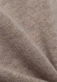 Hellbrauner gestrickter Stoff mit einer weichen, strukturierten Oberfläche. Die Webart weist subtile Variationen und ein flauschiges Finish auf.